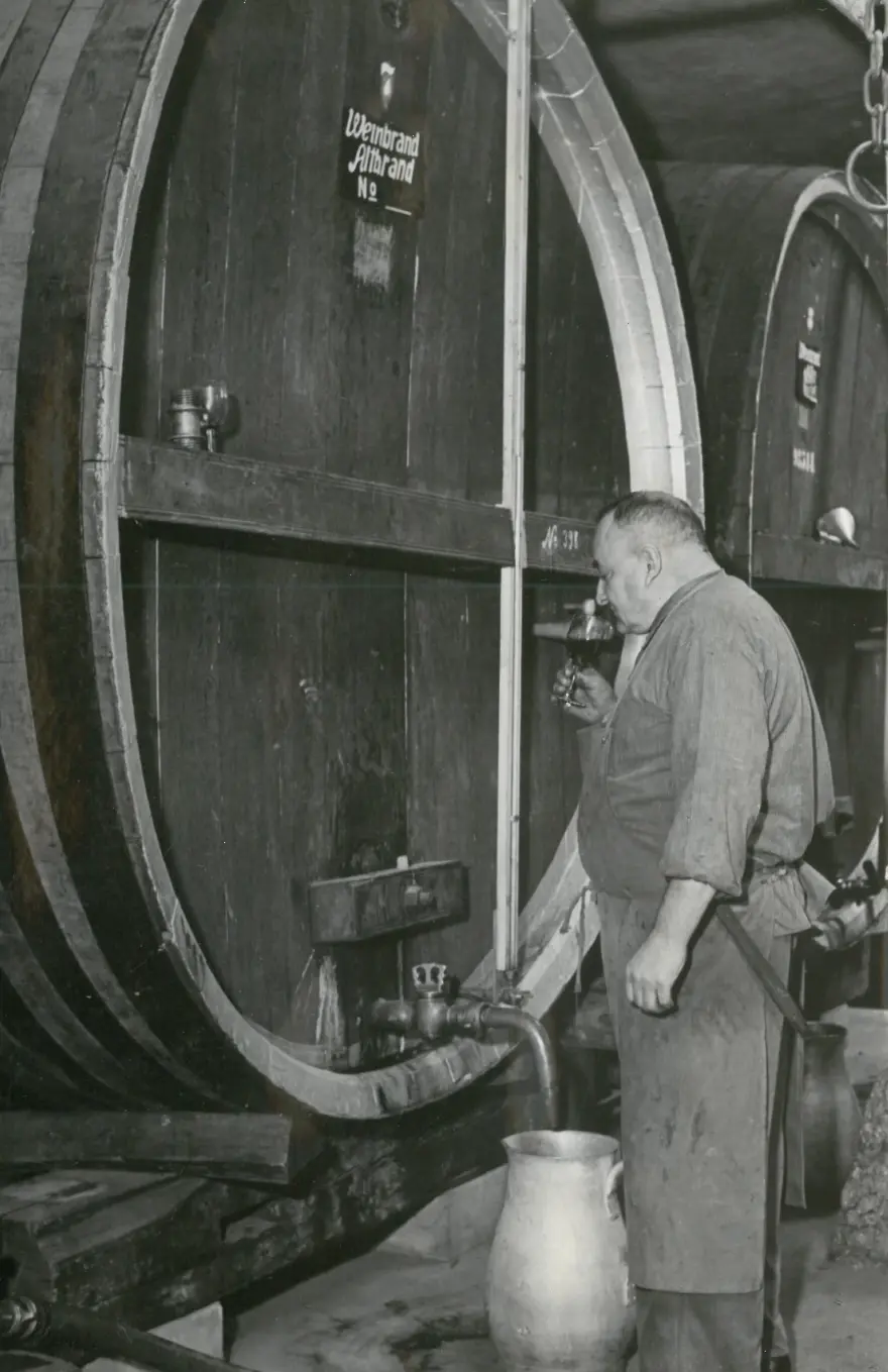 Cellar master drawing brandy from a large wooden cask, historic photo